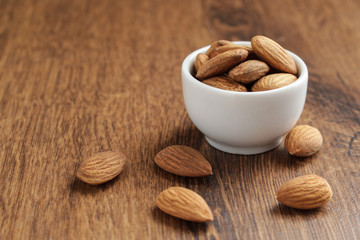almonds in white bowl on brown wooden table with copy space