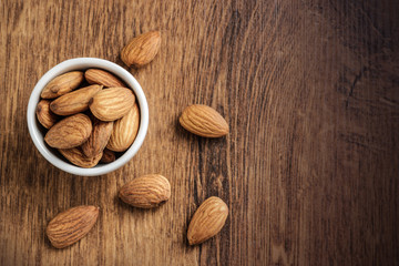 almonds in bowl and scattered on wooden background top view flat lay copy space