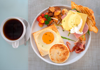 American breakfast with sunny side up eggs, bacon, toast, bread, croissant and coffee on table