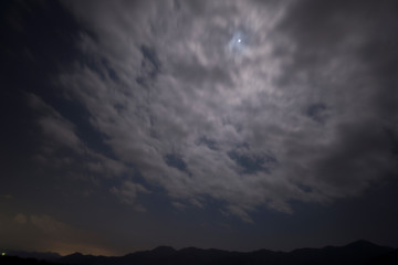 Obraz premium 躍動感のある雲に隠れた月と原っぱ