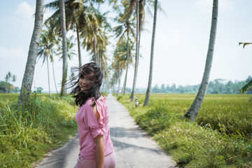 attractive asian woman walking in the middle of empty countryside road  with coconut trees in hot summer day
