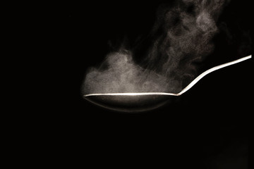 hot steel spoon on black background with steam from water