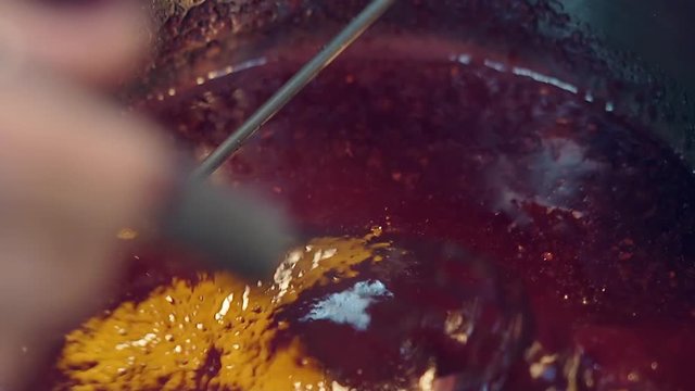 macro confectioner slowly prepares red berry caramel in metal saucepan using small whisk and cooking thermometer