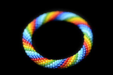 Kid's roll-on rainbow bracelet made of seed beads isolated on a black background close up