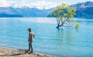 Fototapeta na wymiar Shot of young man wearing hoodies and standing on the bank of lake Wanaka with iconic lone tree. South island of New Zealand.