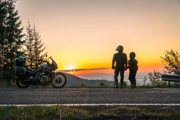 Obraz premium Silhouette of biker couple girl man and adventure motorcycle on the road with sunset light. Top of mountains, tourism motorbike, vacation active lifestyle, happy together. Transfagarasan, Romania.