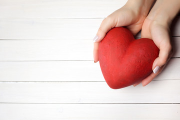 Woman holding hands red heart on white wooden background, top view