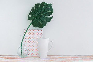 White cup, dotted notebook, retro camera and palm leaf in vase on white background with copy space.