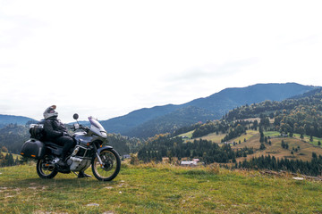 A motorcyclist resting with his touristic motorcycle, with big bags ready for a long trip, black style, white helmet, ride, adventure, outdoor activities, mountains road, Romania