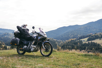 Fototapeta na wymiar A motorcyclist resting with his touristic motorcycle, with big bags ready for a long trip, black style, white helmet, ride, adventure, outdoor activities, mountains road, Romania