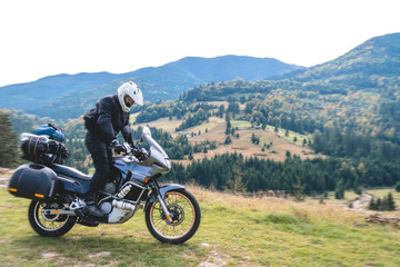 A motorcyclist ride on his touristic motorcycle, with big bags ready for a long trip, black style, white helmet, ride, adventure, outdoor activities, mountain road in Romania