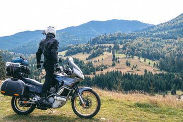 Fototapeta premium Rider man look to distance on his touristic motorcycle, with big bags ready for a long trip, black style, white helmet, ride, adventure, outdoor activities, mountains road, Romania