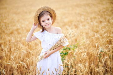 Happy child in autumn wheat field. Beautiful girl in white dress and straw hat have fun with playing, harvesting wheat.