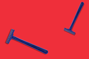 Pair of male disposable plastic razors blue color with two sharp blades on red table in bathroom with copy space for your text. Top view. Hygiene concept