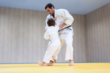 Judo kid and his trainer engaged in judo class in a dojo. Trainer teaches child the methods and...