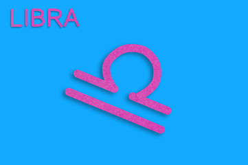 Symbol of astrological sign and word libra cut out of purple paper on blue table. Top view. Horoscope concept