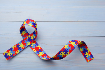 World Autism awareness and pride day or month with Puzzle pattern ribbon on blue wooden background.