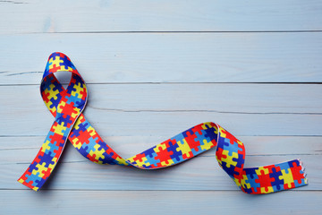 World Autism awareness and pride day or month with Puzzle pattern ribbon on blue wooden background.