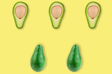 Rows of fresh wholes and halves of organic avocado with kernels in center of yellow table in kitchen or market. Top view. Cooking concept