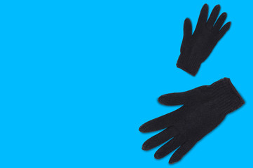 Obraz premium Pair of black warm woolen gloves on blue background with copy space for your text. Top view