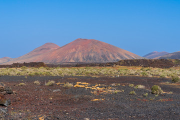 Fototapeta na wymiar Spain, Lanzarote, Red volcanoes behind endless fields of volcanic soil