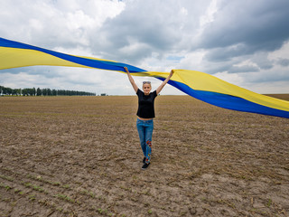Young amazing beautiful girl with a huge Ukrainian flag on the field. Ukraine's Independence Day.