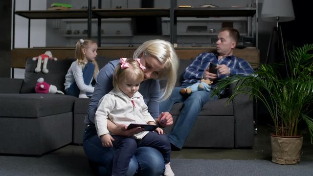 Modern Family Using Smart Technology Devices Separately From Each Other. Mother With Toddler Daughter Watching Cartoon On Cellphone, Father Networking On Smart Phone, Preschool Girl Feeling Abandoned.