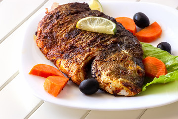 Grilled fish sea bream with vegetables on white plate. White background. Healthy diet food concept.