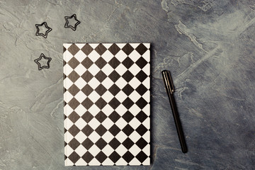 Black paper clips, pen and closed black-white colored copybook on dark black abstract background...