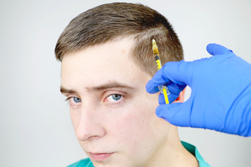 Hair mesotherapy or hair transplant: a beautician doctor makes injections in the man’s head for...
