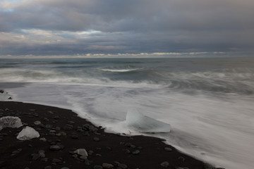Dramatic a sunset with amazing transparent blue iceberg pieces on Diamond beach with black sand near Jokulsarlon lagoon, Iceland. Ice calving. Water long exposure.
