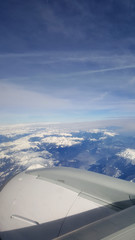 Fototapeta na wymiar flying and traveling abroad, bird eye view from airplane window on the jet wing on cloudy blue sky iceberg mountain aboard morning winter time, journey backgrounds