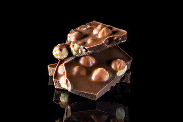 Pieces of chocolate with whole nuts on black reflective background.