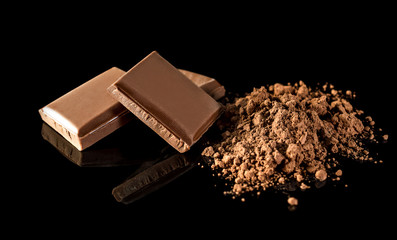 Pieces of chocolate bar with heap of cocoa powder on black.