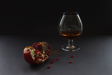 A glass of cognac and pomegranate. Still life. Dark background