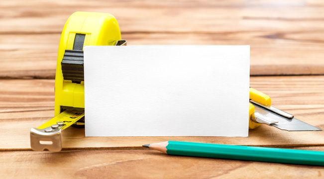 Blank business card with measuring tape tool, stationery knife and pencils on the table. Business template.