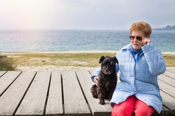 portrait of senior woman sitting with her dog on a beach board