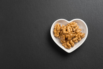 A few shelled walnuts lie in a saucer in the shape of a heart on textured slate board