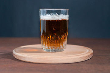 Light beer in a high glass glass on a wooden stand on brown wooden background