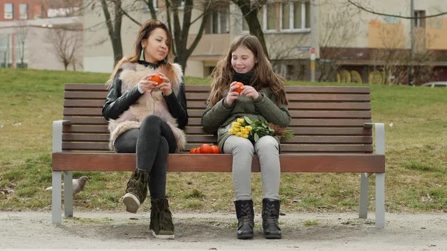 Young mother with kid daughter girl sit on bench peel and eat tangerines enjoy beeing together and hug