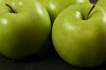 Green apples on black board - closeup photo with detail on skin texture.