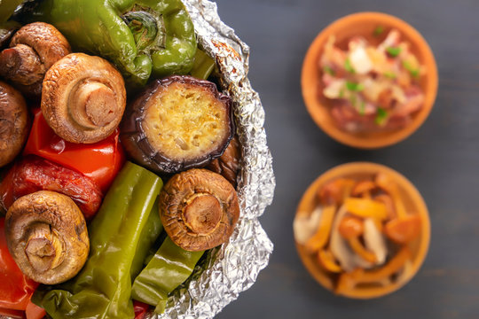 Baked vegetables in foil - tomatoes, eggplants, peppers on a gray wooden table background. View from above. Close-up