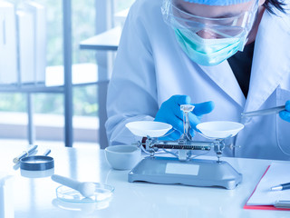 Fototapeta premium Close up, an asian chemist or scientist researcher using mechanical scale for gathering and measuring specimen at laboratory. The young man wearing safety glasses in experiment.