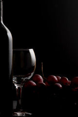 Wine glass and bottle with  red grapes on a dark. Space for text