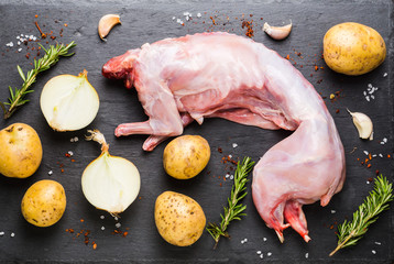 Raw rabbit meat on the black stone board with other ingredients. Selective focus.