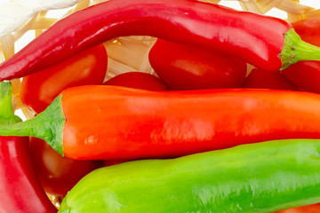 large pods of red hot pepper a piece of a long green vegetable in a tomato basket close-up