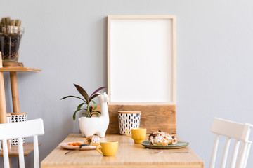 Naklejka na ściany i meble Stylish and sunny interior of kitchen space with small wooden table with mock up photo frame, design cups and tasty dessert. Scandinavian room decor with kitchen accessories, cacti and plants.