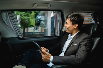 asian young businessman with tablet sitting on passenger seat of his luxury car