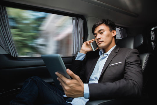 man in suit sitting on passenger seat using tablet pc and calling by phone