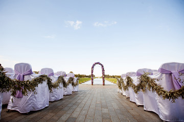 Obraz na płótnie Canvas Beautiful wedding. The round arch is decorated with flowers and greenery, the ceremony on the seashore. Guest chairs are decorated with bows, elegant furnishings, sunny day.
